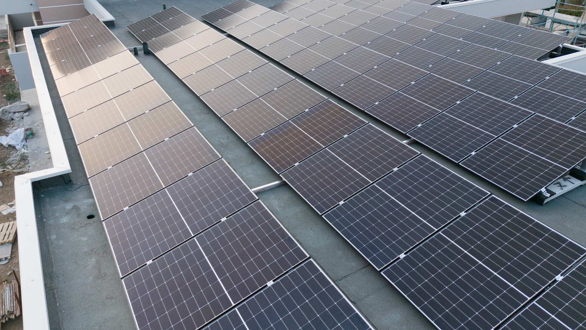 File di pannelli fotovoltaici su una copertura piana, ripresi dall'alto da un drone con la luce radente del tardo pomeriggio